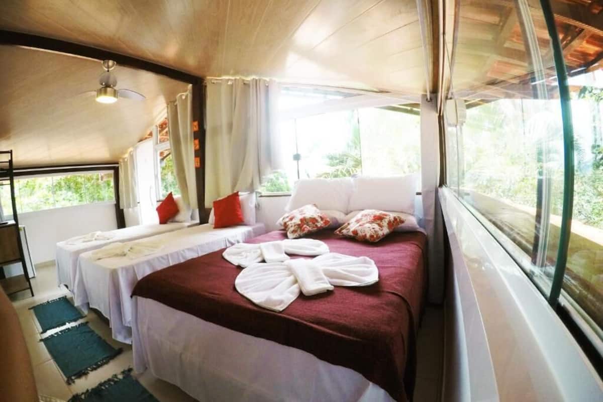 Una habitación con una cama, dos mesitas de noche, un ventilador de techo y una ventana con cortinas.