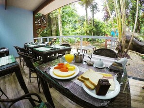 An outdoor dining area with tables and chairs, a breakfast spread including toast, fruit, and a hot beverage. - Pousada Guapuruvu (Angra dos Reis)