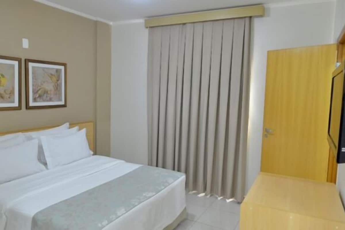 A hotel room with a bed, a desk, a curtain, and two framed pictures on the wall.