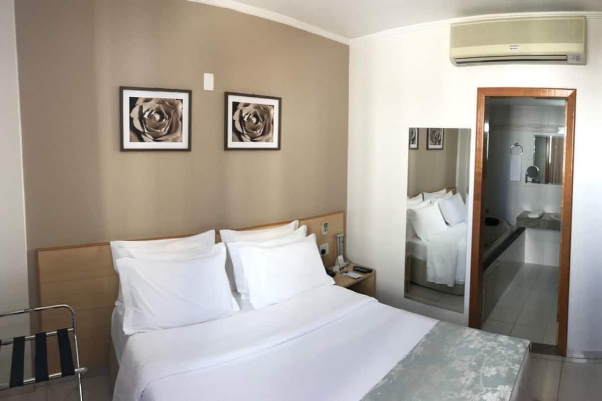 A hotel room with a bed, a nightstand, a mirror, and a door.
