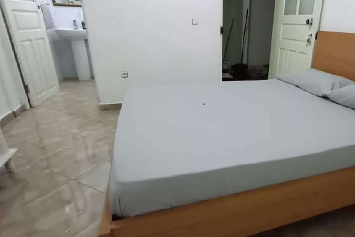 A single-bed room with a wooden headboard, a white mattress, and a grey pillow.