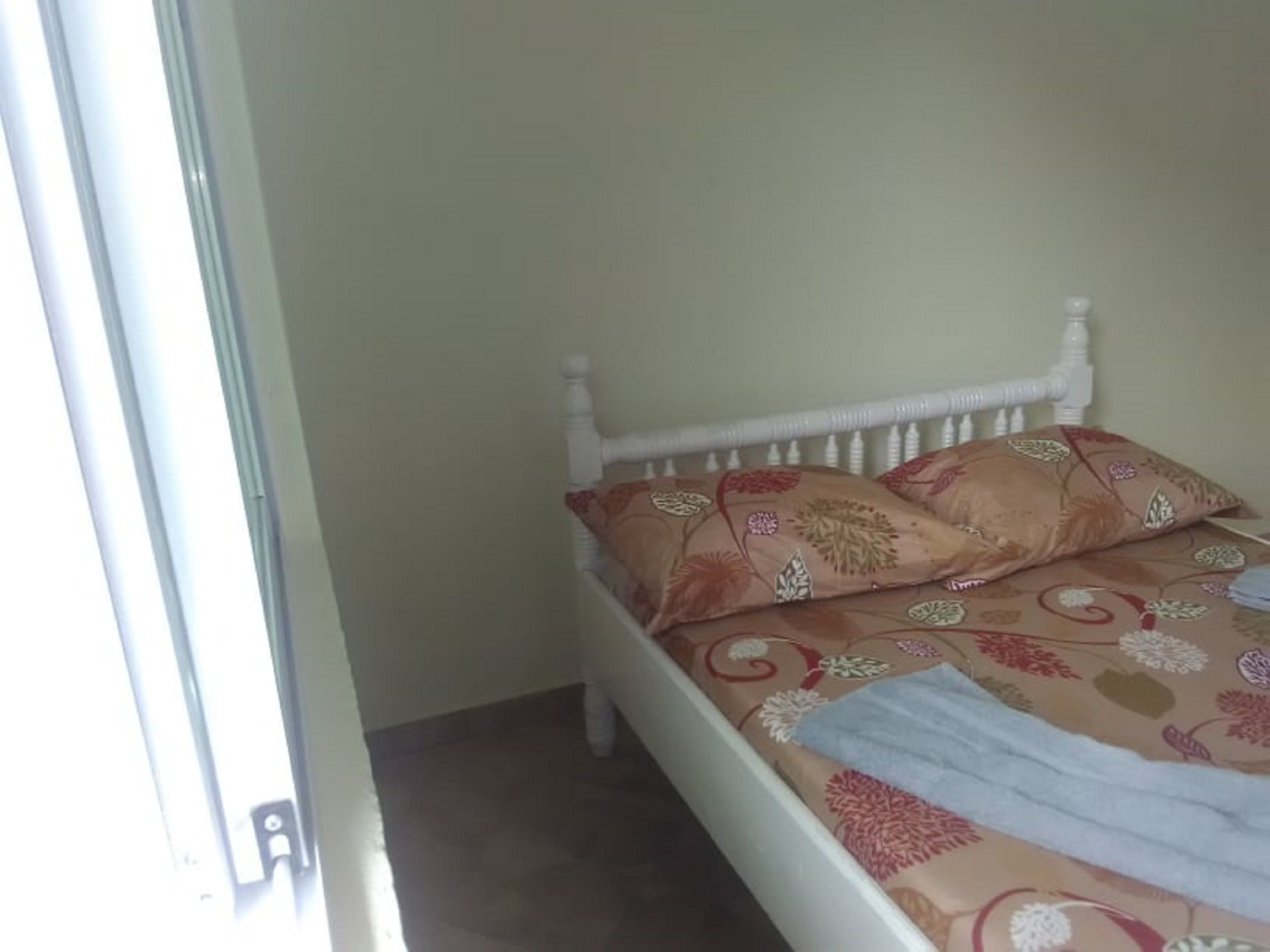 A bed with a floral bedspread and two pillows, a white headboard, and a window with blinds.