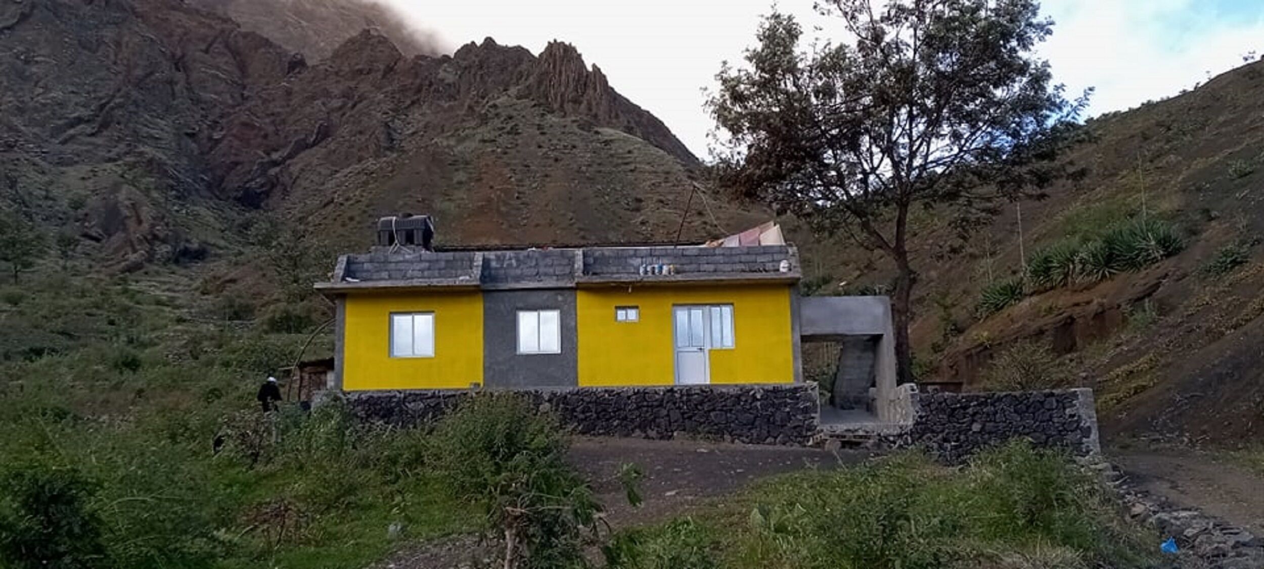 A yellow building with a stone foundation, set against a mountainous backdrop.
