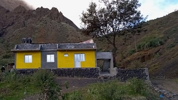 A yellow building with a stone foundation, set against a mountainous backdrop.