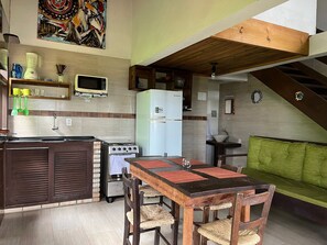 A compact kitchen with a dining area, a refrigerator, a stove, and a microwave. - Pousada Vale Verde Bungalows (Imbituba)