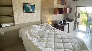 A bedroom with a bed, a shelf with towels, a painting, a microwave, and a view of the outdoors. - Pousada Vale Verde Bungalows (Imbituba)