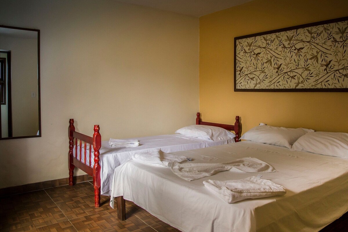A double bed with white linens and two pillows, a wooden headboard, and a wall-mounted artwork.