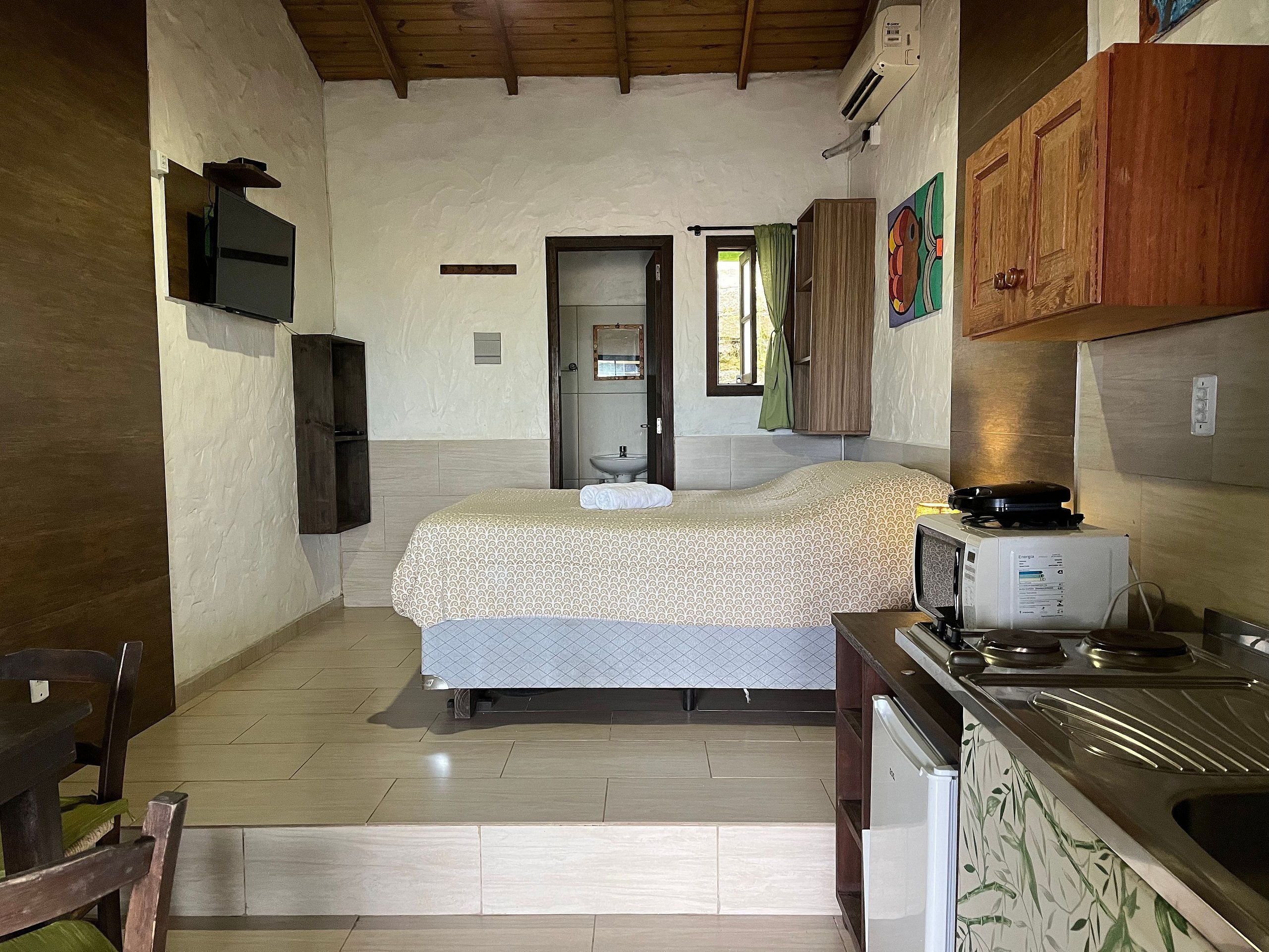 A compact bedroom with a bed, a small kitchenette, and a bathroom.