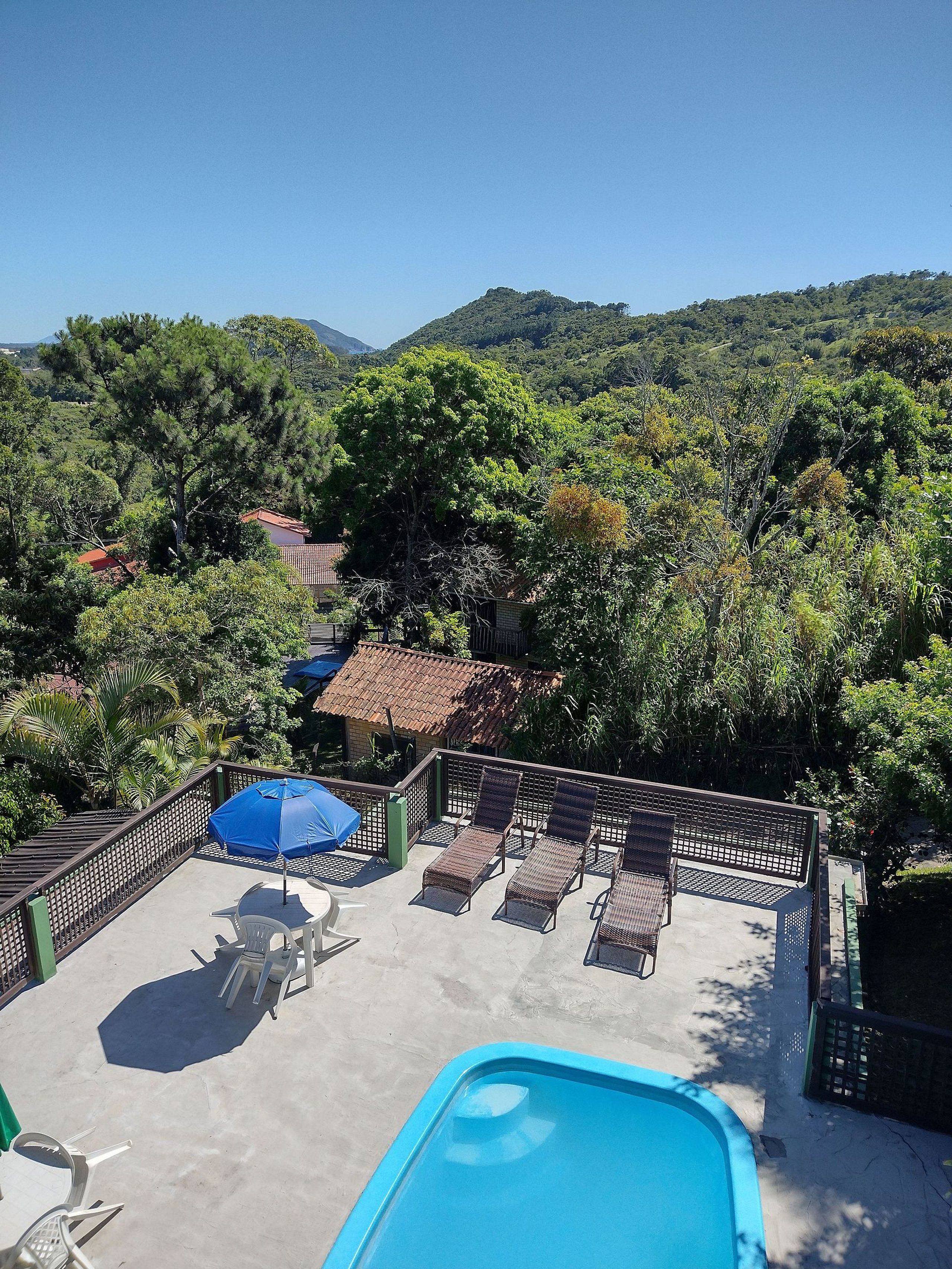 Zona junto a la piscina con sillones de descanso y sombrillas, rodeada de vegetación exuberante y colinas al fondo.