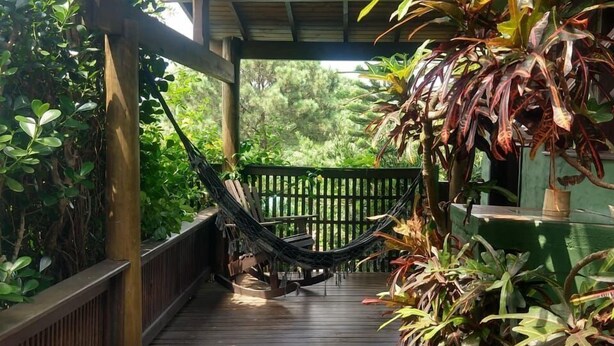 A wooden deck with a hammock, surrounded by lush greenery and a wooden fence. - Pousada Vale Verde Bungalows (Imbituba)