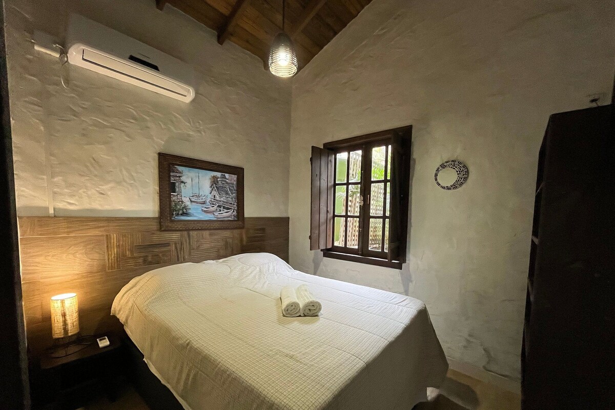 A bedroom with a wooden headboard, a painting, a window, and a bedside lamp.