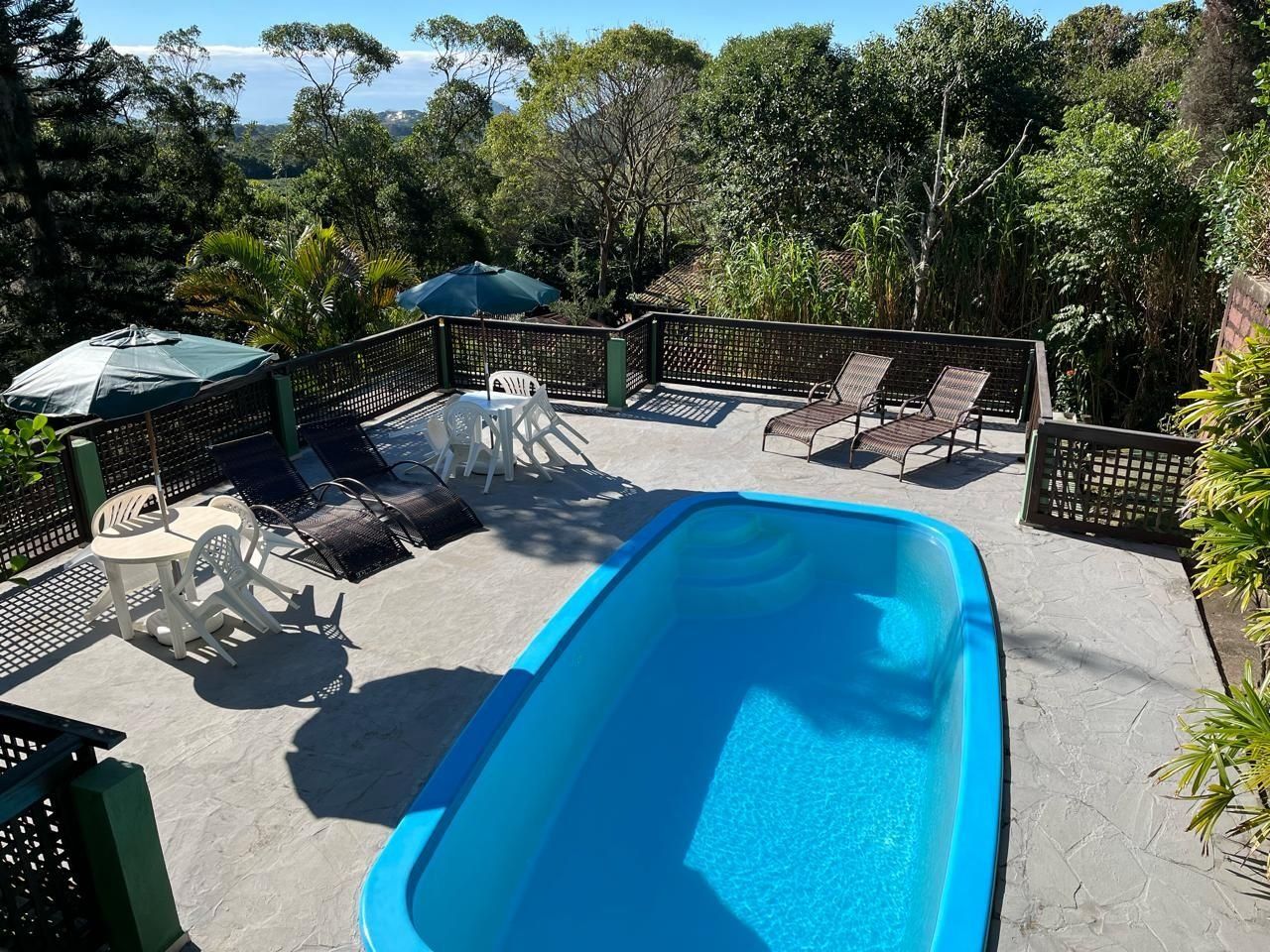 A rectangular swimming pool with lounge chairs and tables around it, surrounded by a fence and greenery.