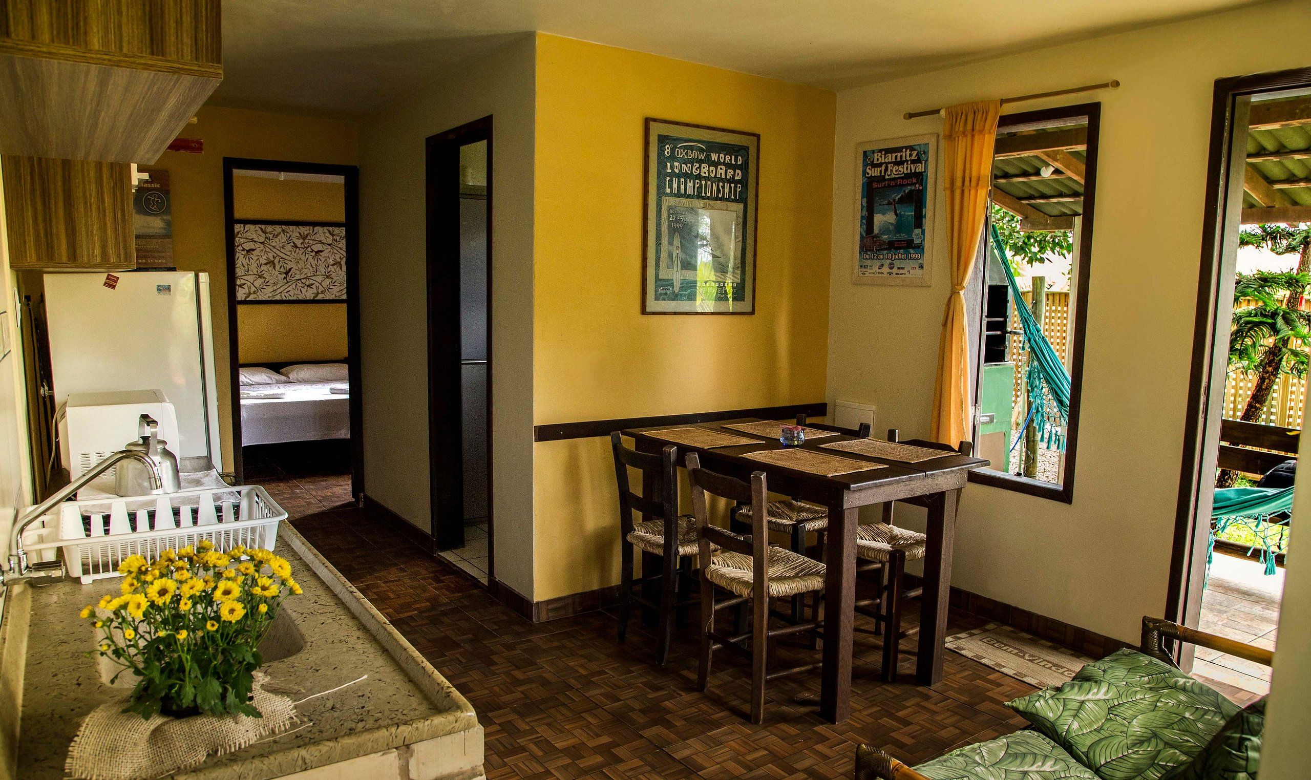 Quarto de hotel pequeno com uma cama, uma mesa para refeições e cadeiras, uma pia com torneira e uma janela com cortinas.