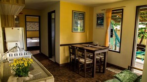 A compact hotel room with a bed, a small dining table with chairs, a sink with a faucet, and a window with curtains. - Pousada Vale Verde Bungalows (Imbituba)