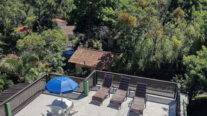 A poolside area with lounge chairs and umbrellas, surrounded by lush greenery and hills in the background. - Pousada Vale Verde Bungalows (Imbituba)