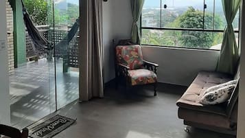 Quarto com sofá, uma cadeira, janela com vista para área verde e rede do lado de fora.
