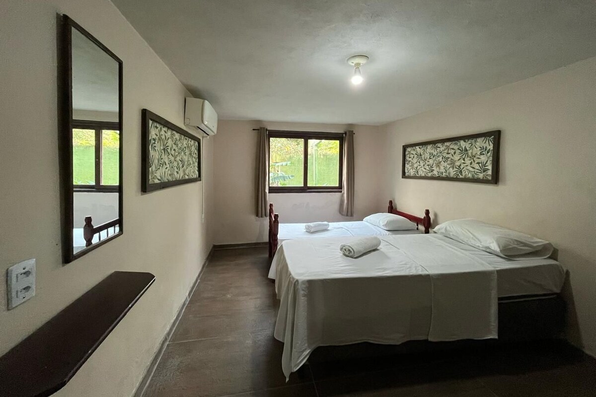A hotel room with two beds, a bench, a window, and a ceiling light.