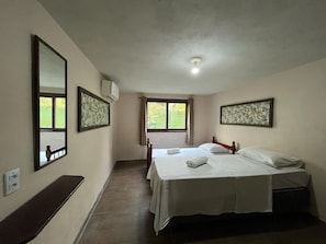 A hotel room with two beds, a bench, a window, and a ceiling light. - Pousada Vale Verde Bungalows (Imbituba)