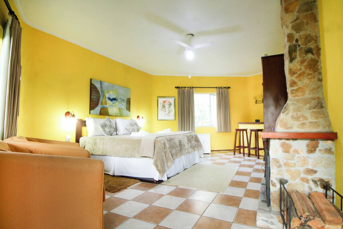 Un dormitorio con cama, chimenea de piedra, suelo a cuadros y pared amarilla.
