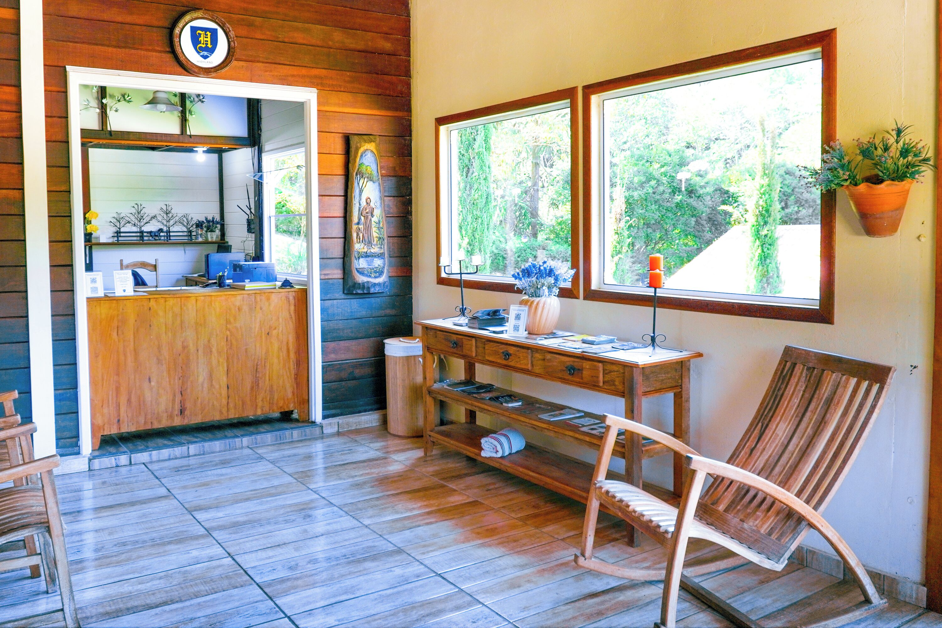 Um interior em madeira com uma mesa de recepção, uma cadeira, uma pequena mesa e uma janela com uma planta.