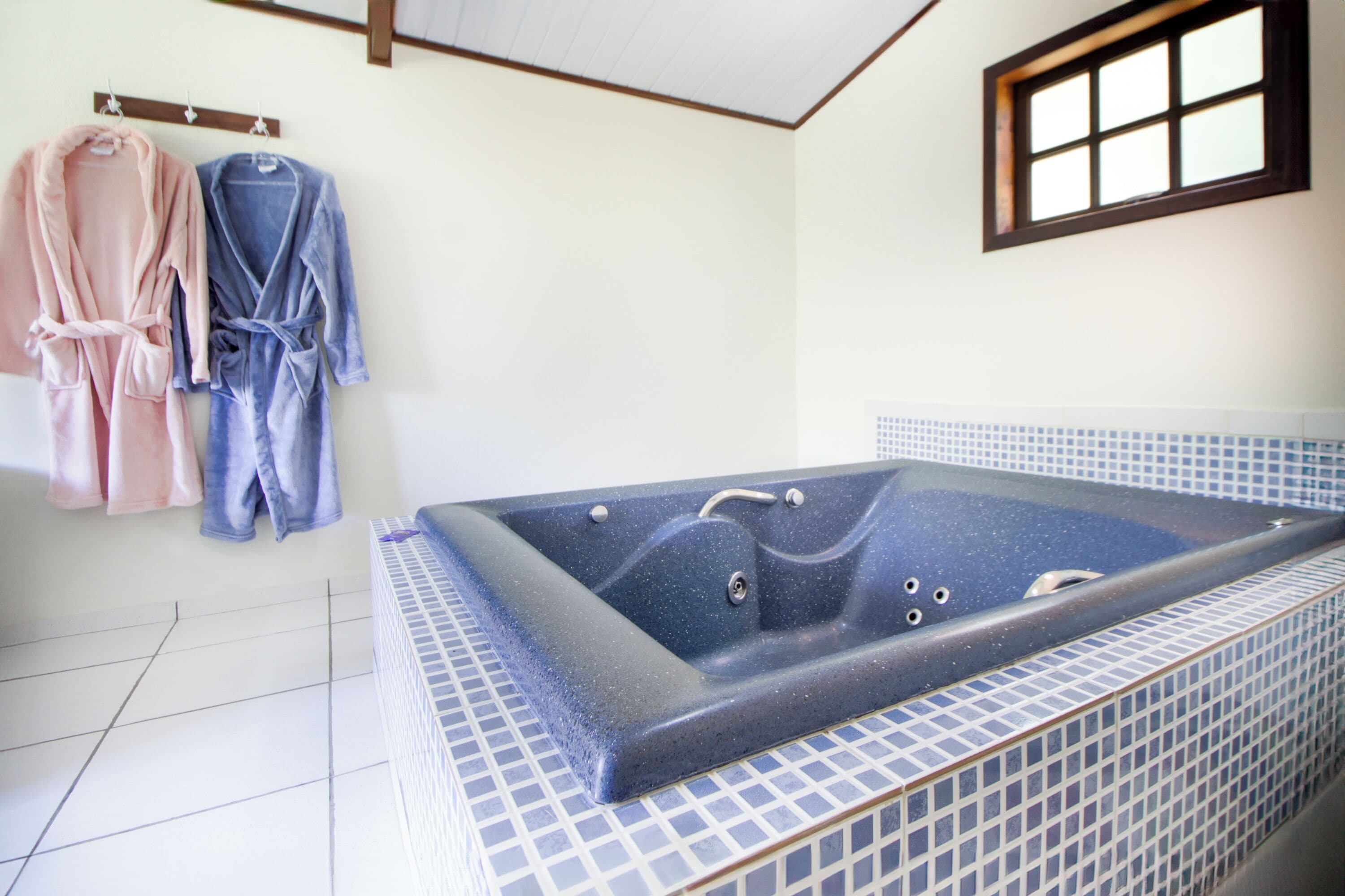 Casa de banho com uma banheira grande, chão em azulejos e dois roupões pendurados num porta-toalhas.