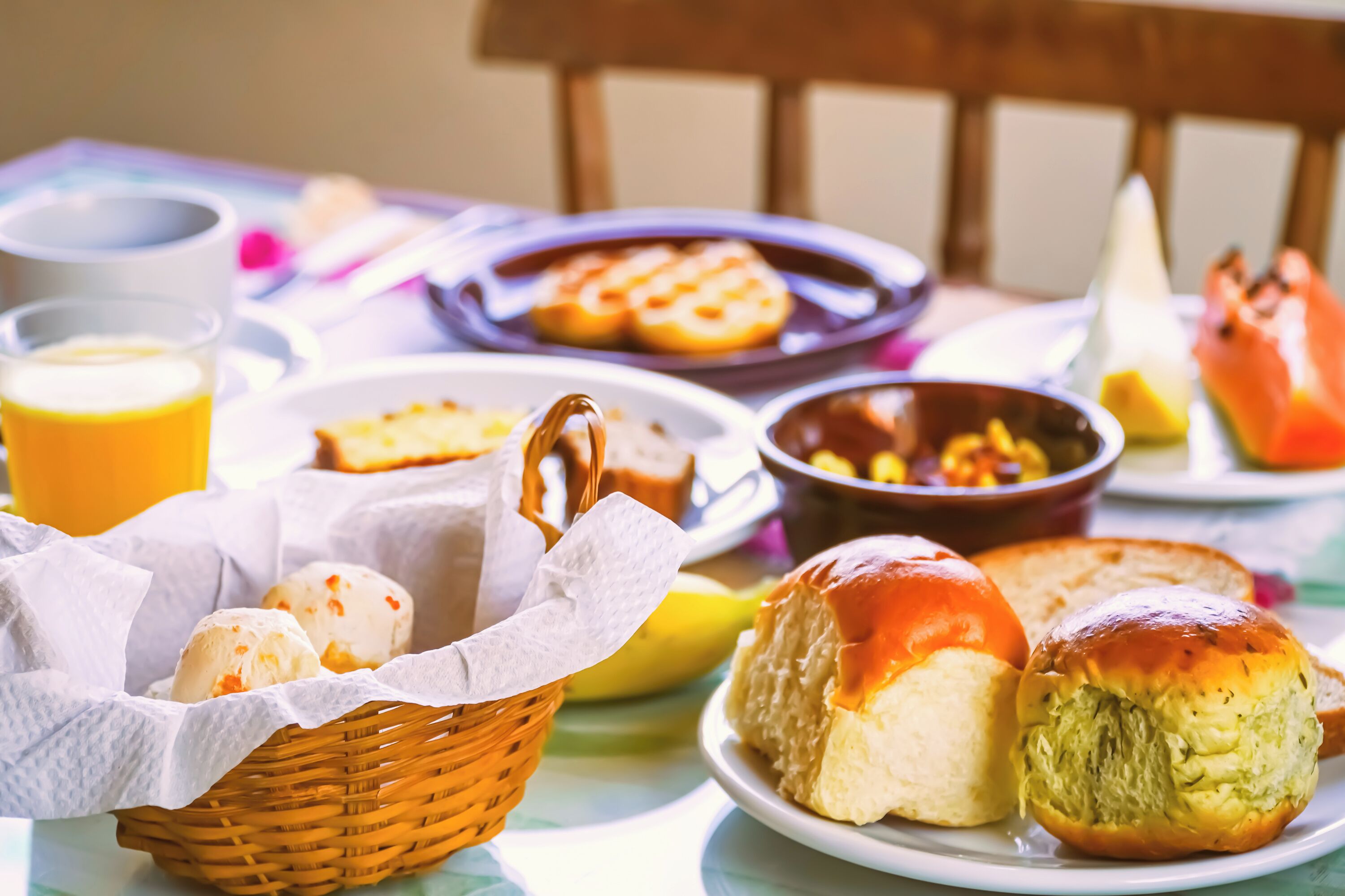 A breakfast setting with various pastries, a glass of orange juice, and a bowl of corn.