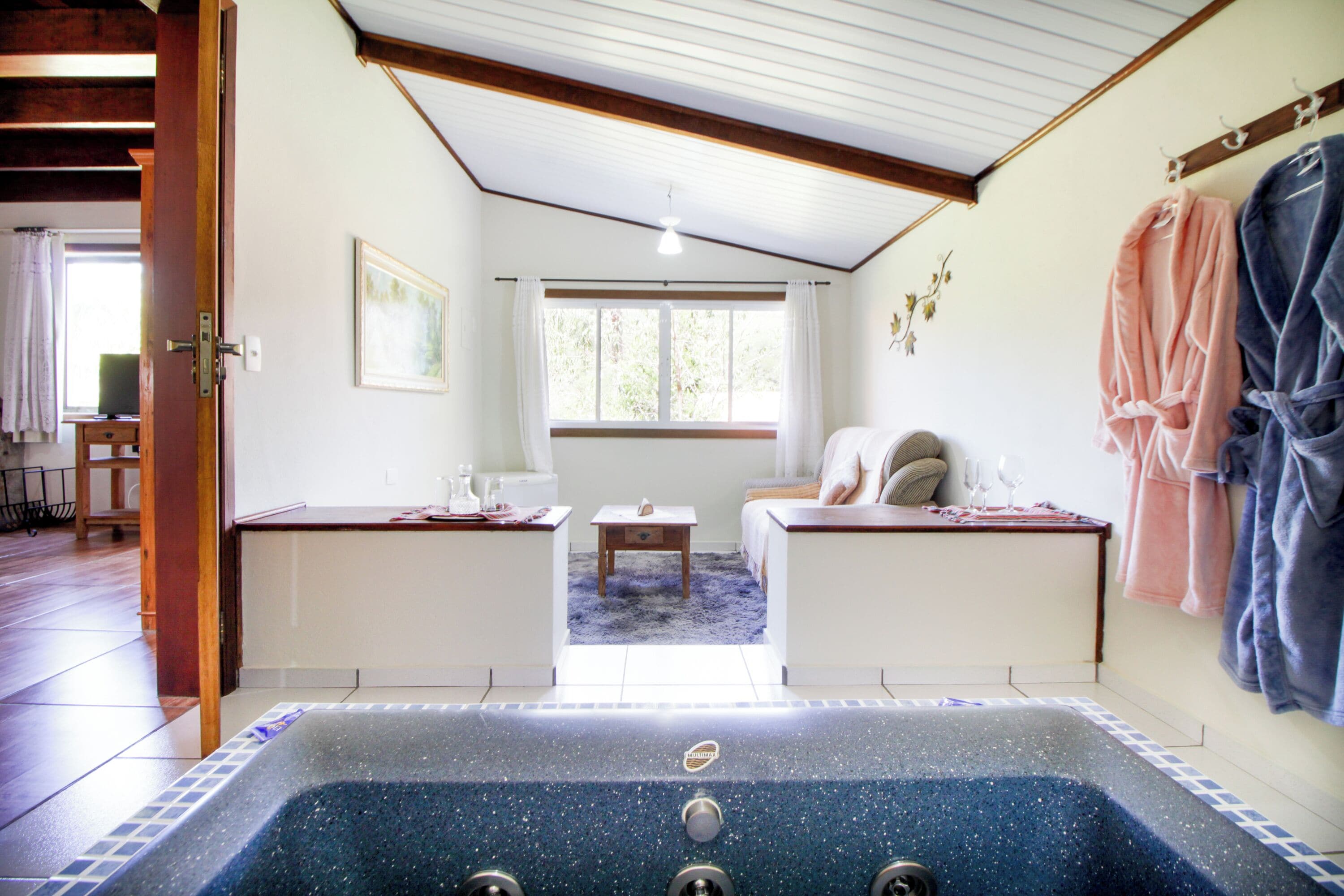 Una habitación con un jacuzzi grande, techo de madera, ventana con cortinas y cama con alfombra azul.