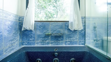 A bathroom with a large bathtub, a window with white curtains, and blue tiled walls.