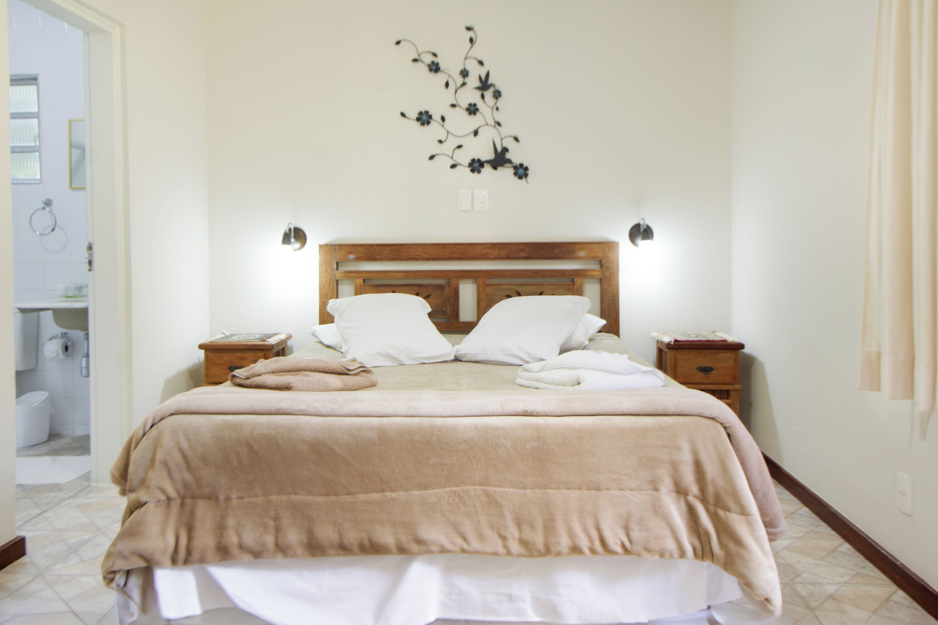 Un lit bien fait, avec une tête de lit en bois, deux tables de chevet et un luminaire fixé au mur.