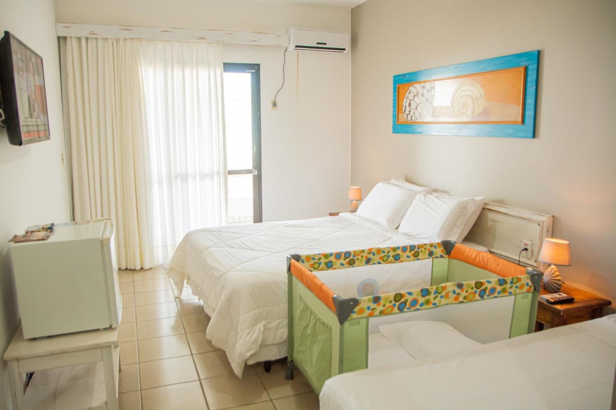 A hotel room with a bed, a small table, a chair, a desk, and a window with curtains.