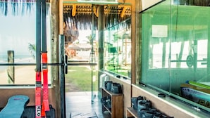 A gym with exercise equipment, a wooden bench, a mat, and a view of the beach.
