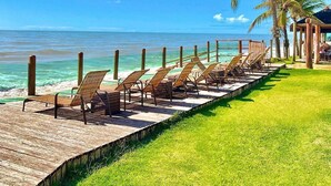 A wooden deck with lounge chairs facing the ocean, palm trees, and a clear blue sky.