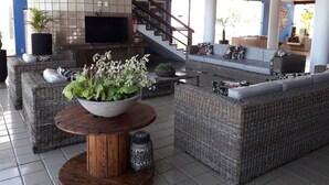 A spacious indoor area with wicker furniture, a large TV, and a staircase leading to an upper level.