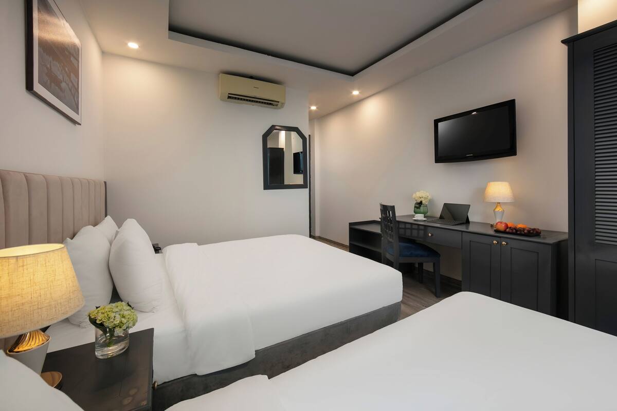 A hotel room with two beds, a desk, a chair, a TV, and a lamp.