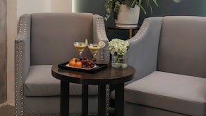 A modern lounge area with two grey sofas, a small round table with a tray of fruits and drinks, and a large decorative wall with floral patterns. - Hanoi La Palm Boutique Hotel (Hanoi)