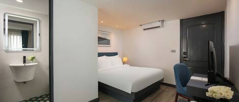 A hotel room with a bed, a desk, a chair, a small table with a vase of flowers, a sink, and a mirror.