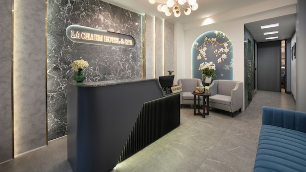 A modern hotel reception area with a marble wall, a reception desk, and a seating area with a blue sofa and a chair. - Hanoi La Palm Boutique Hotel (Hanoi)
