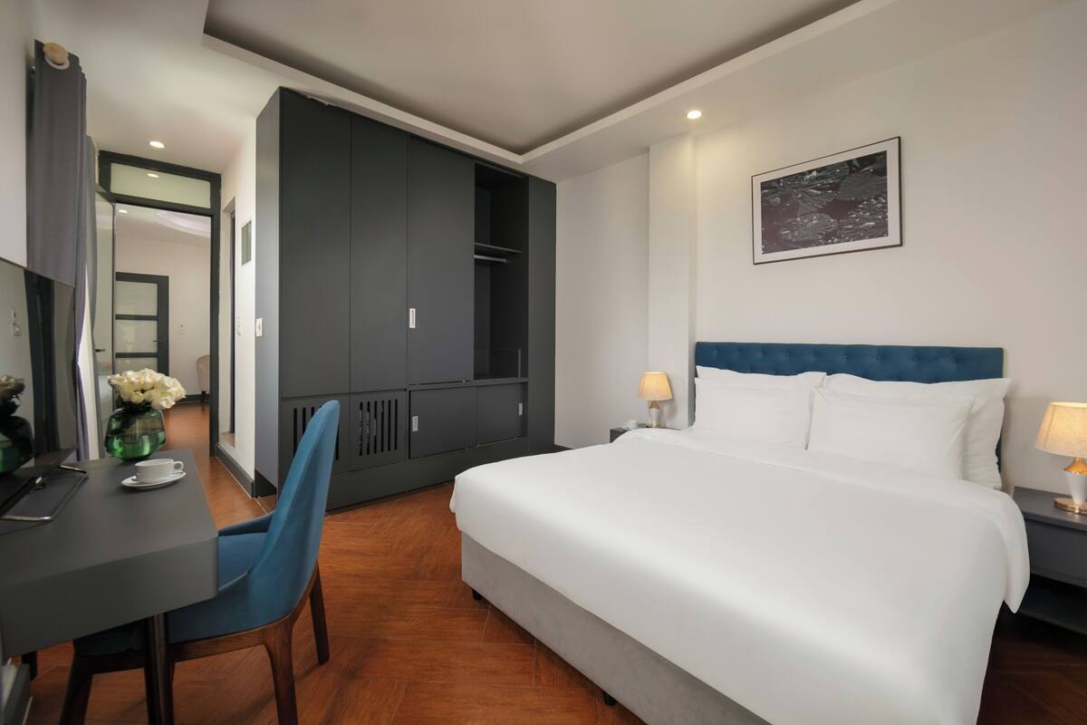 A hotel room with a bed, a desk, a chair, a wardrobe, and a nightstand with lamps.