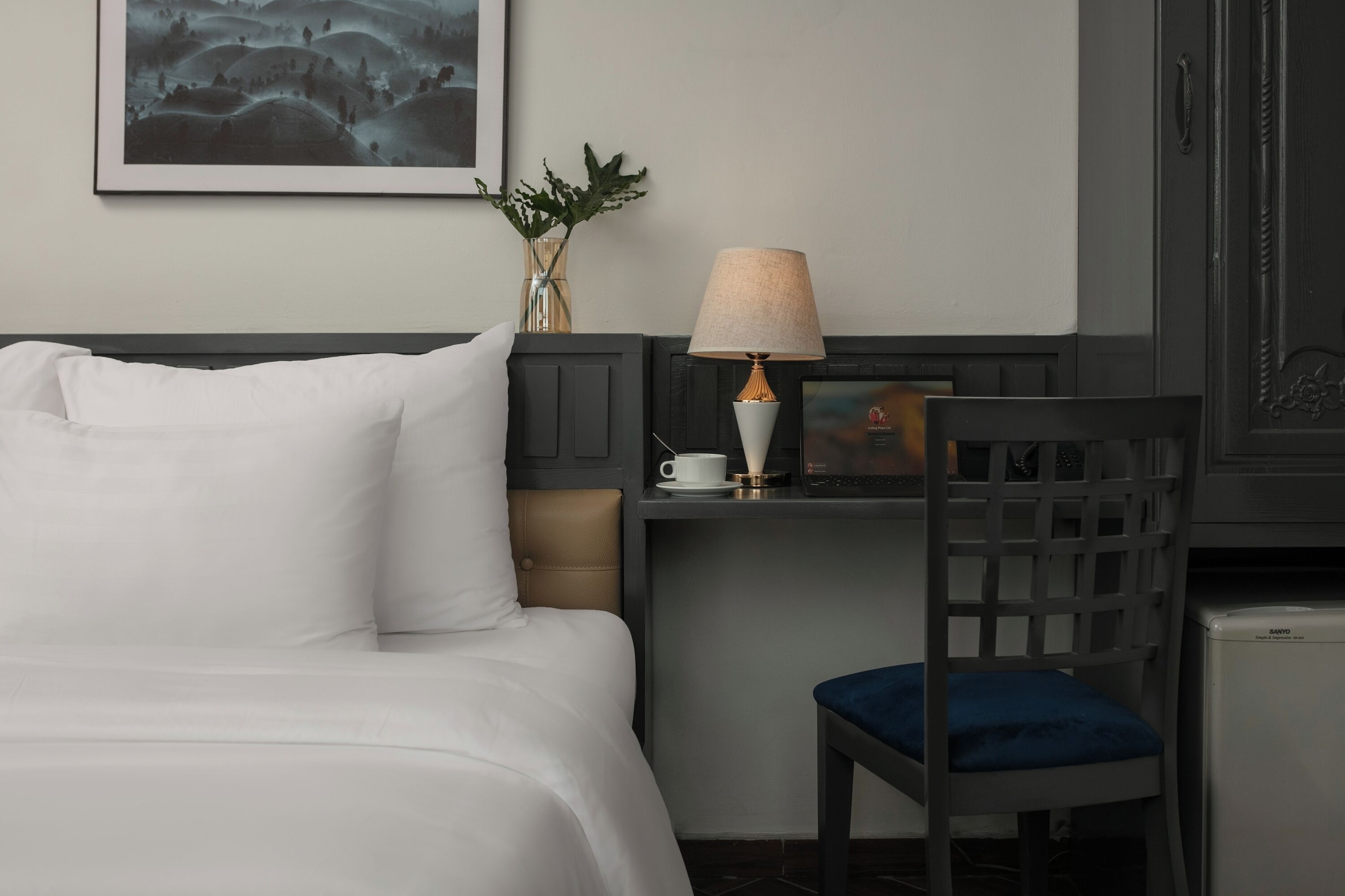 Habitación de hotel con cama, escritorio con lámpara, silla y refrigerador pequeño.