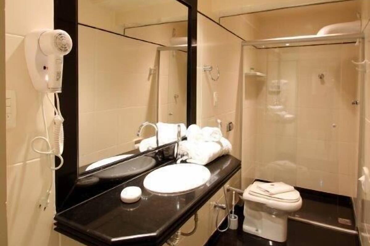 Une salle de bain moderne équipée d’un grand miroir, d’un sèche-cheveux, d’un lavabo et de toilettes.
