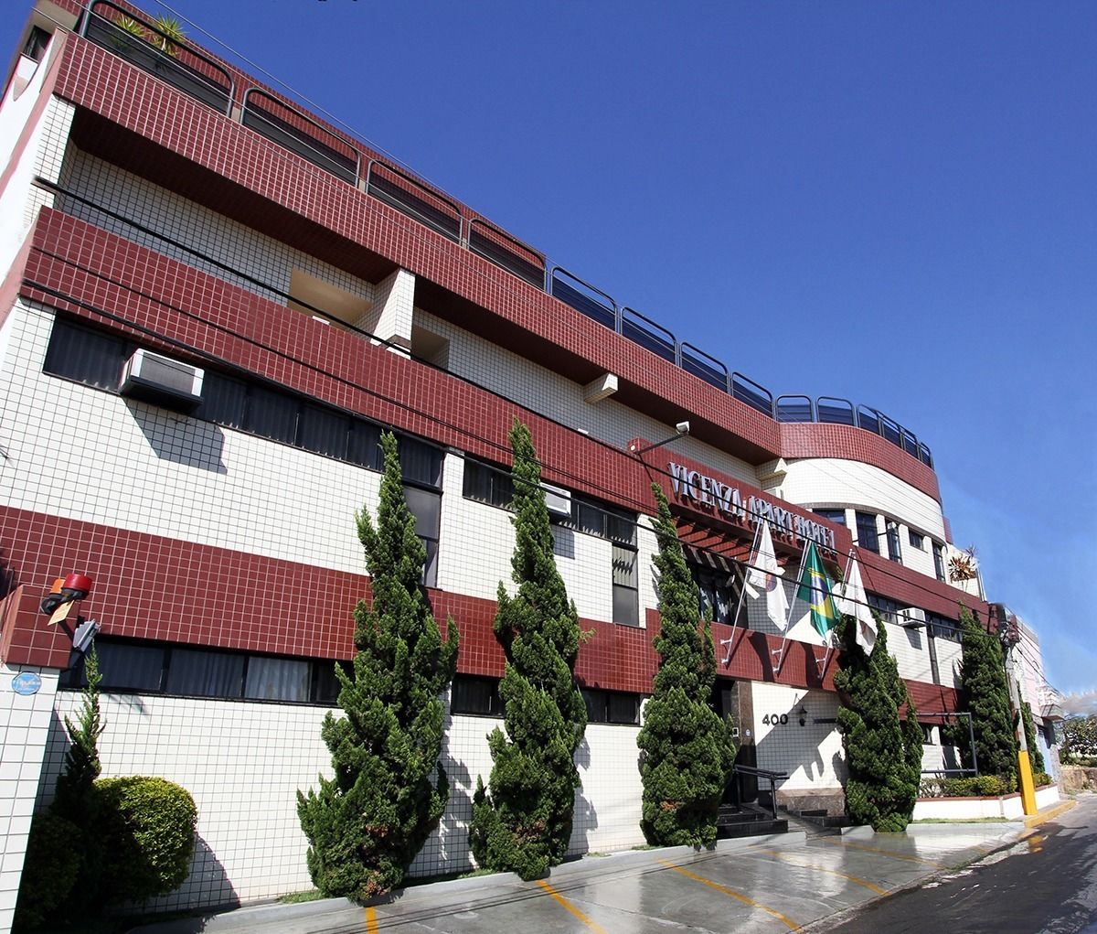 Un hotel de varios pisos con fachada roja y blanca, balcones y banderas.