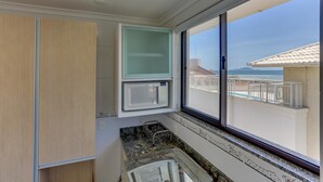 A kitchen with a microwave, a sink, and a window overlooking a balcony. - Pousada Costão dos Ingleses (Florianopolis)