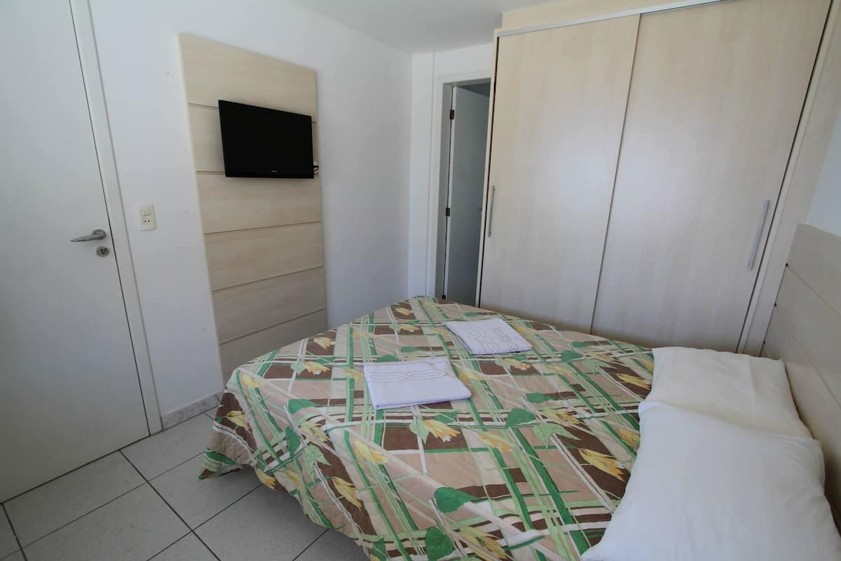 A small, clean room with a bed, a television mounted on the wall, and a wardrobe.