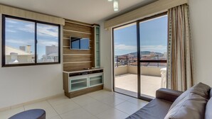 A modern living room with a large window, a flat-screen TV, and a sliding glass door leading to a balcony. - Pousada Costão dos Ingleses (Florianopolis)