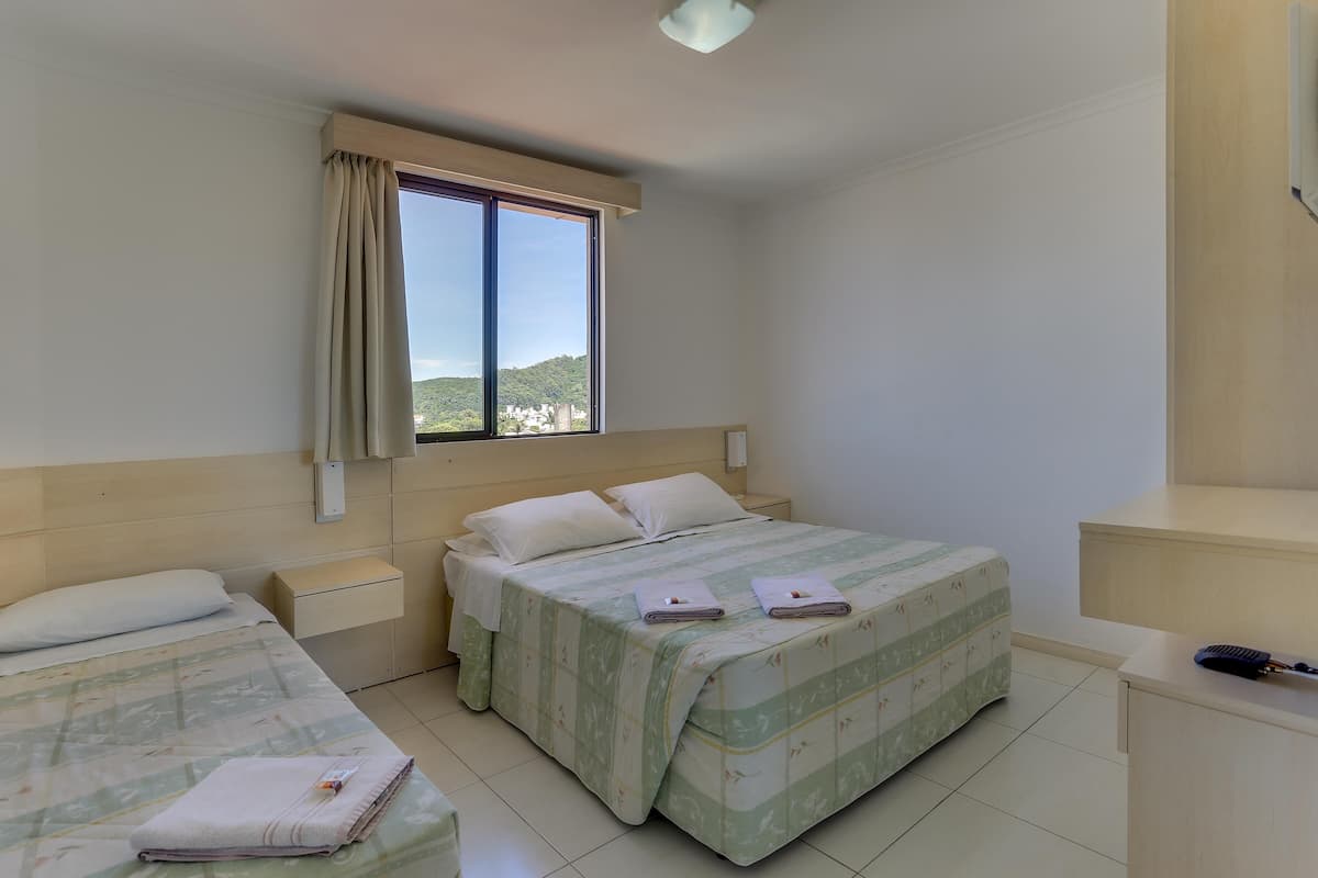 A bedroom with a bed, a nightstand, a desk, and a window with a view of a hill.