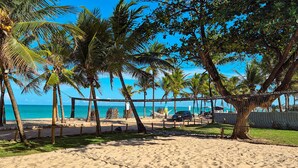 A beach with a volleyball net, palm trees, and a clear blue sky. - Pousada dos Coqueiros (Ipojuca)