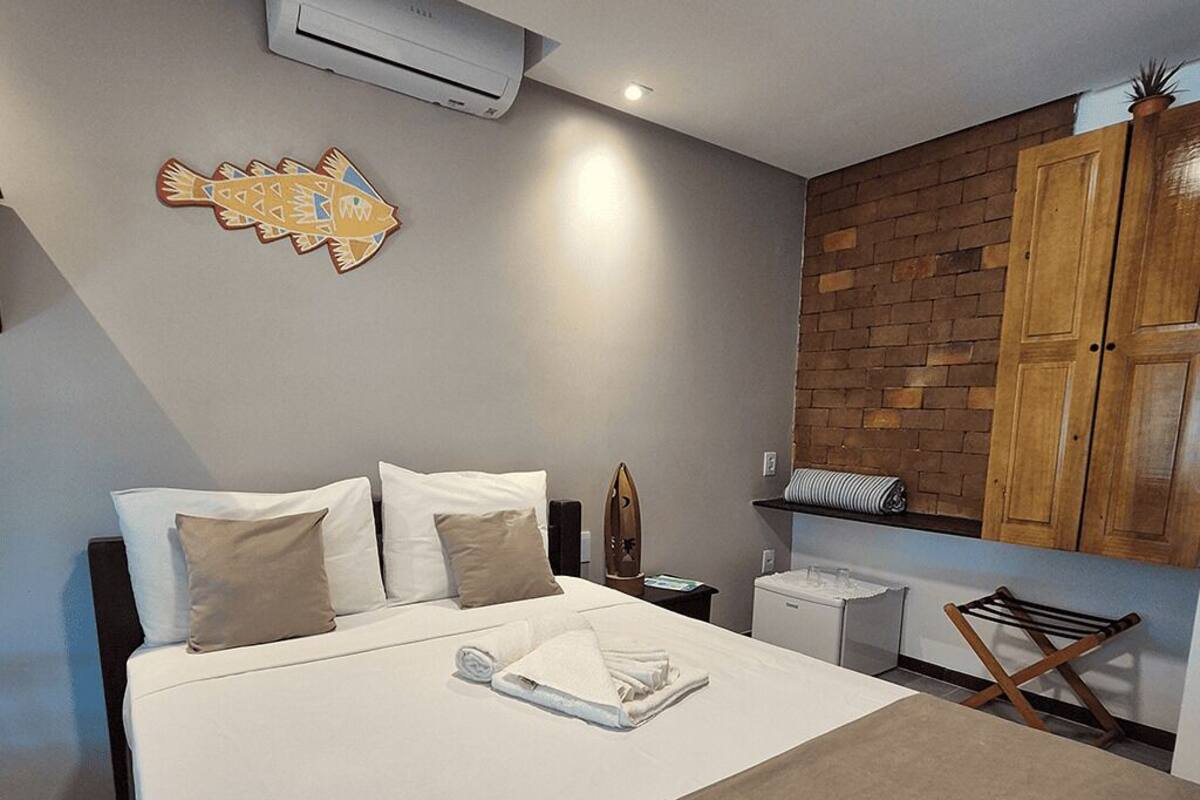 Une chambre d’hôtel avec un lit, des oreillers, un porte-serviettes, une petite table et un mur en briques.