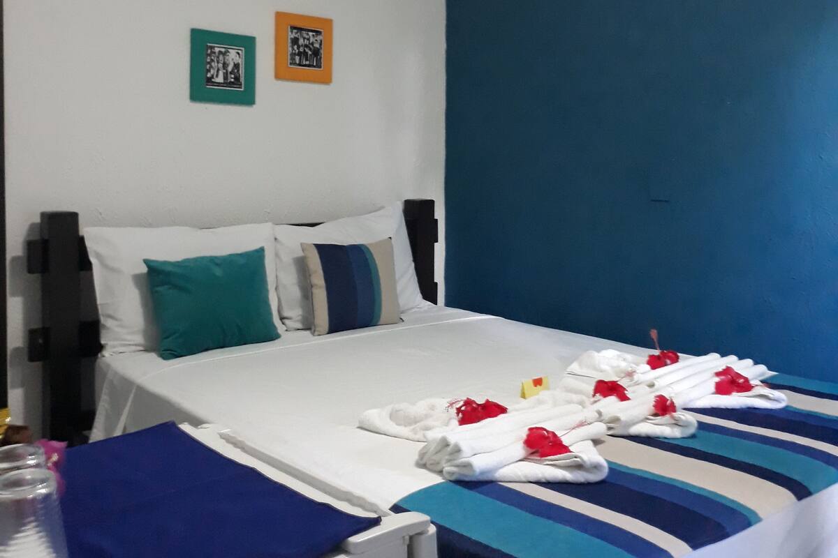 Une chambre d’hôtel comprenant un lit, une table de chevet, une petite table, deux tableaux encadrés accrochés au mur et un appareil de climatisation.