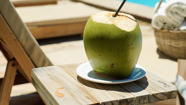 A green coconut drink on a wooden table by a poolside with lounge chairs and a view of the ocean. - Pousada dos Coqueiros (Ipojuca)
