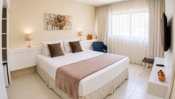 Habitación de hotel con cama, lámparas de noche, una silla, escritorio, televisor y un amplio ventanal con cortinas.